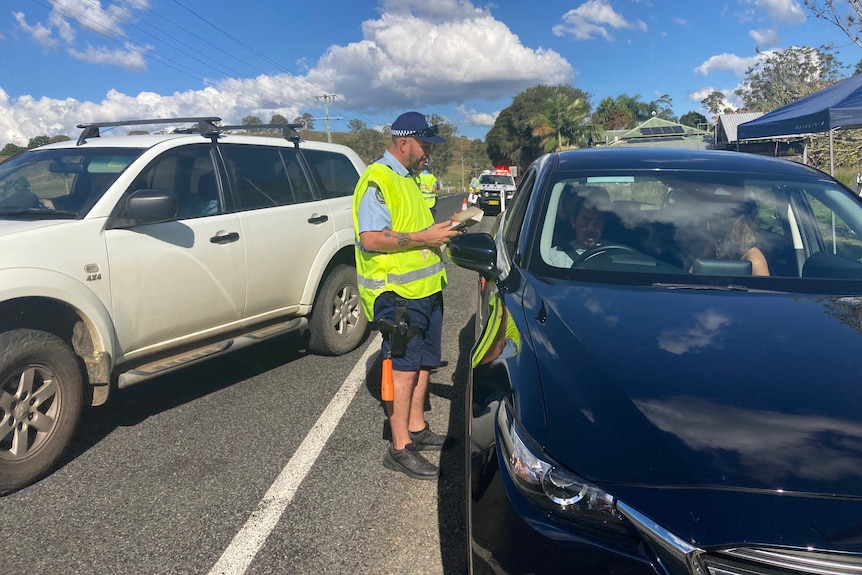 A police officer in a yellow vest talks to a driver during a roadside drug test.