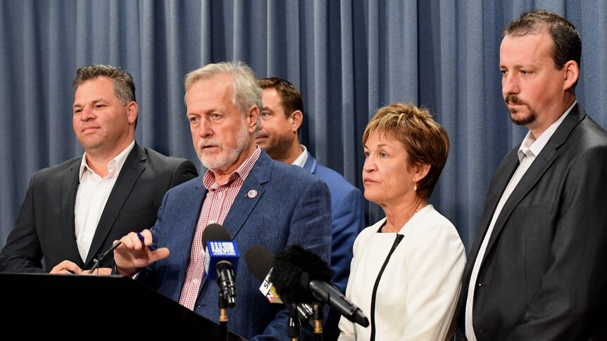 Four men and woman stand in front of microphones