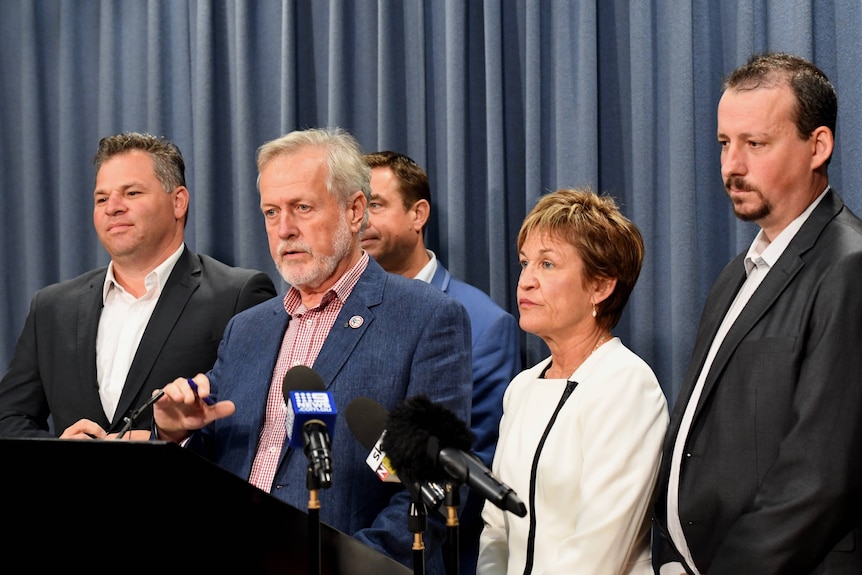 Four men and woman stand in front of microphones
