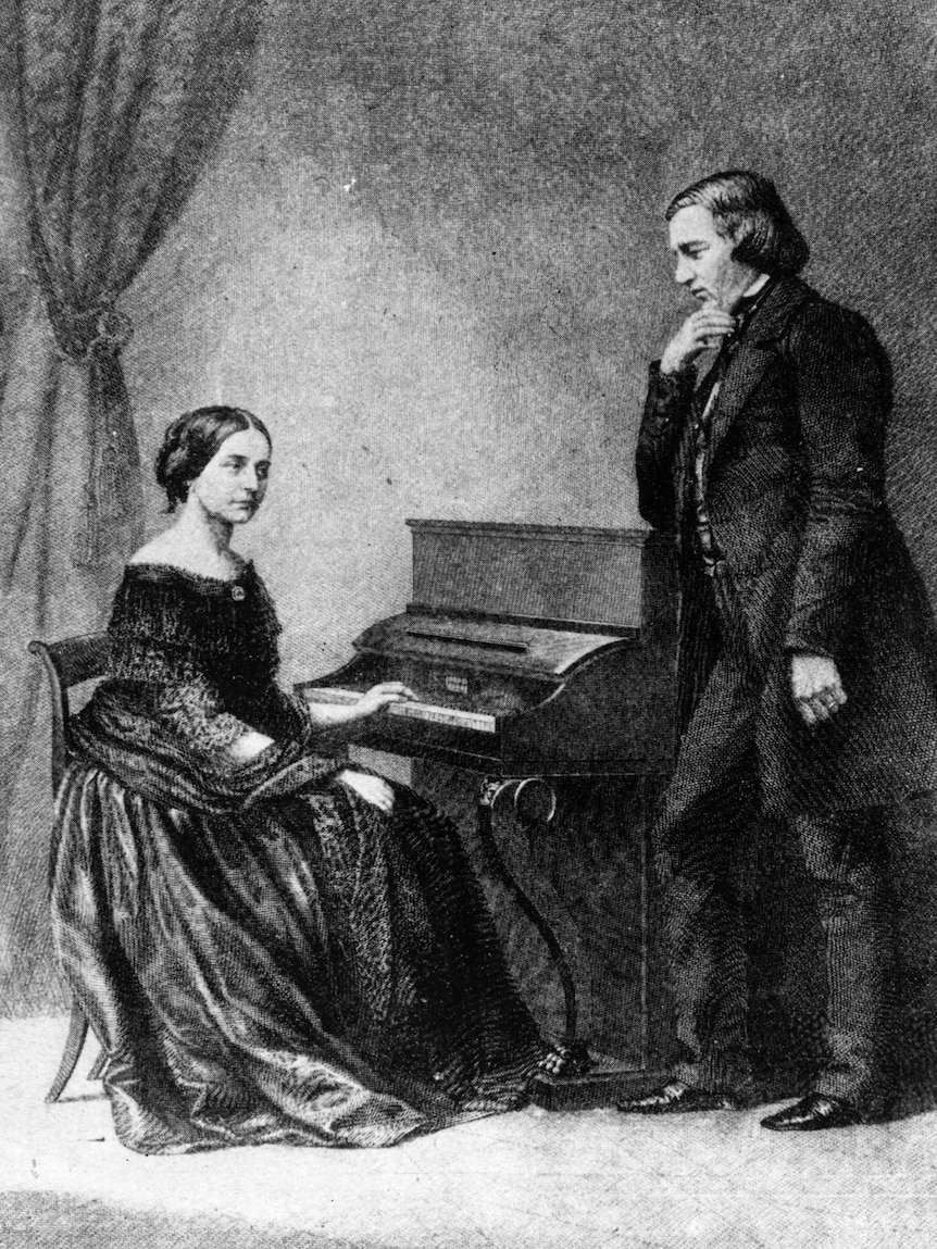 Young woman sits at the piano while a man leans on the piano.