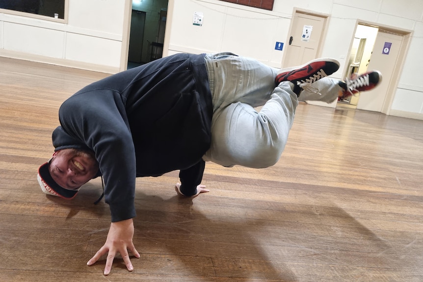 Man wearing jeans and hoodie shows a breakdancing move in a country hall. Ausnew Home Care, NDIS registered provider, My Aged Care