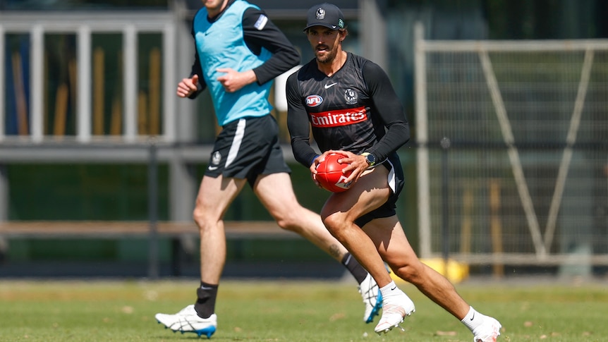 A Collingwood footballer looks up as he holds the ball ready to kick downfield during training.
