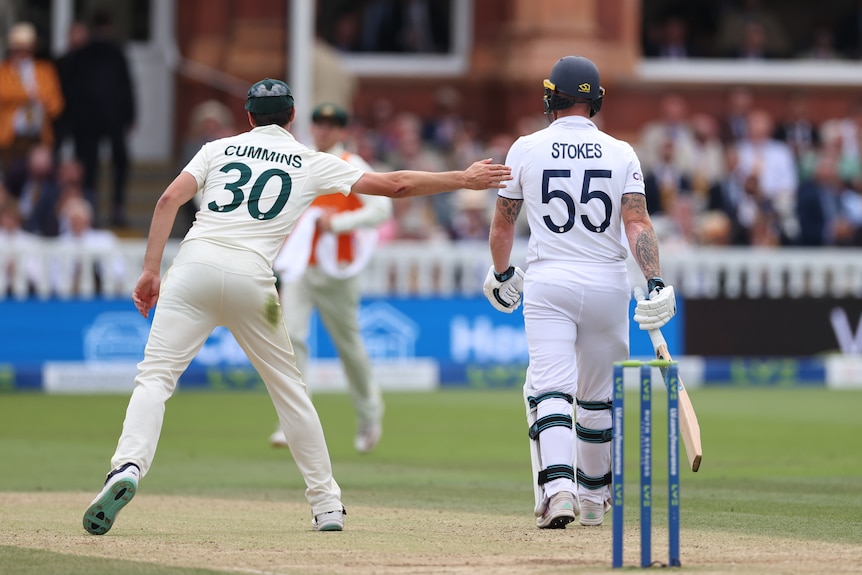Seen from behind, Australia fielder Pat Cummins reaches to pat England batter Ben Stokes after he was dismissed in an Ashes Test