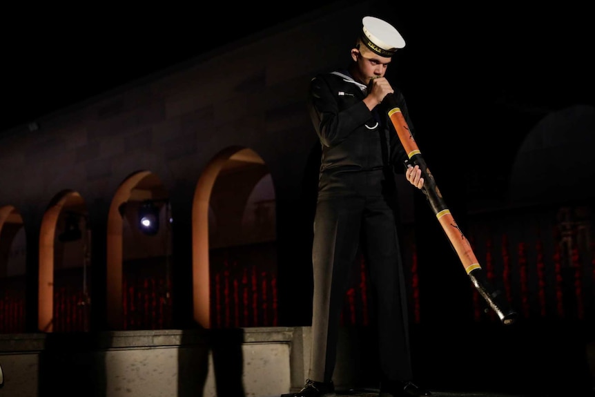 a man in a navy uniform plays the didgeridoo