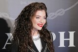 Medium shot of female singer Lorde standing in front of a screen smiling.