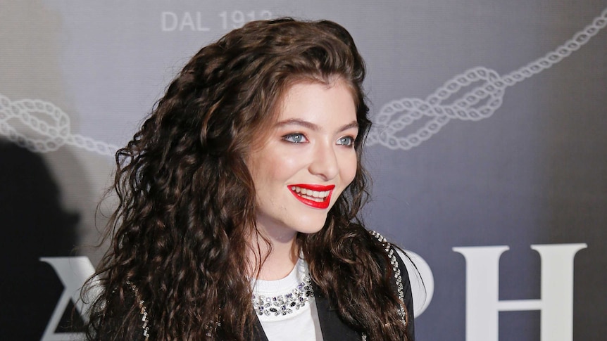 Medium shot of female singer Lorde standing in front of a screen smiling.