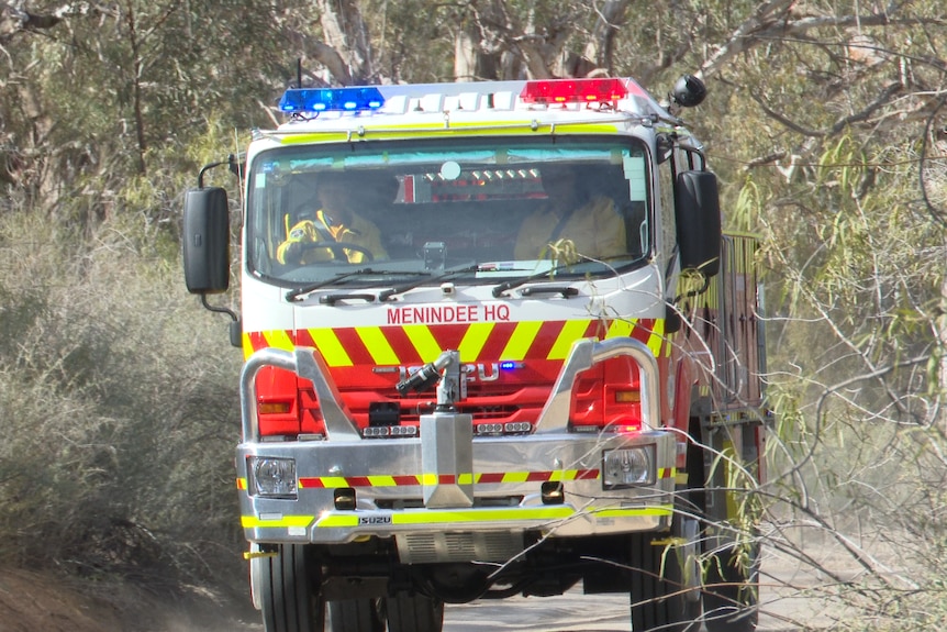 A fire truck driven by one person wearing a yellow jacket, and another RFS volunteer in the front seat with lights flashing