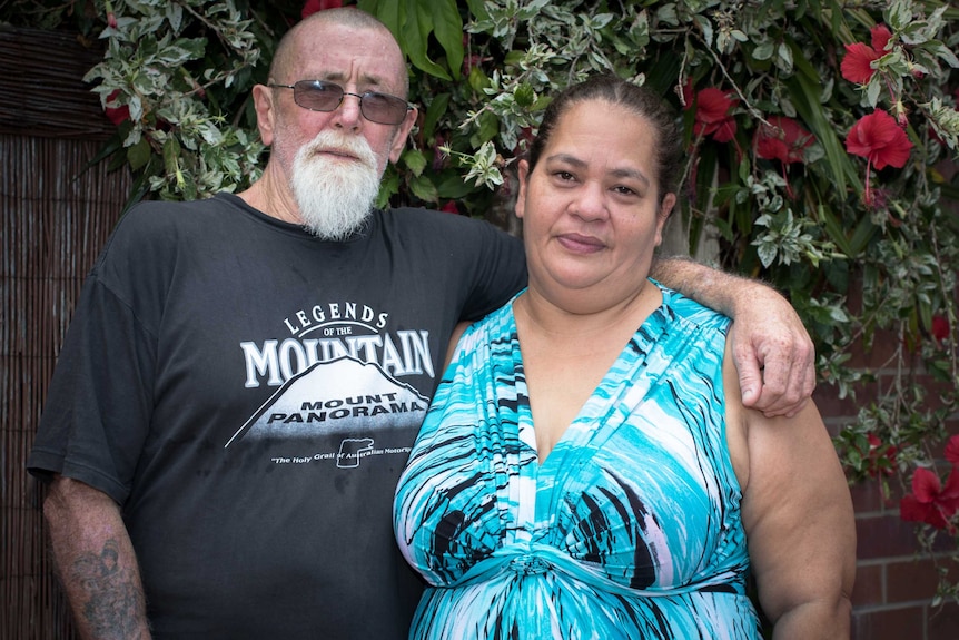 Portait of sol daley with his arm around his wife jennifer joyce, both looking with serious expressions at the camera.