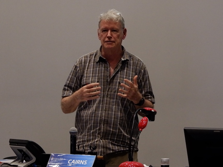 A man speaks in an ill-lit conference room.