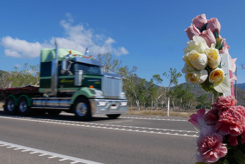 Fake flowers wrapped around a post by the Bruce Highway, a truck passes in the background.