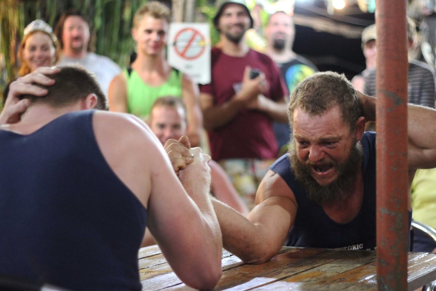 Two men arm wrestle at a table.