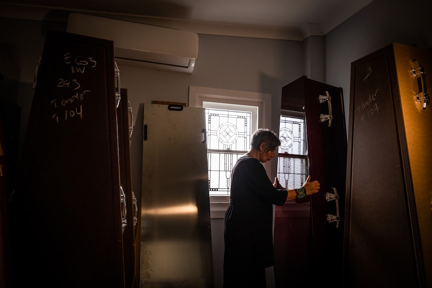 A moody, dark image of a woman arranging various types of coffins