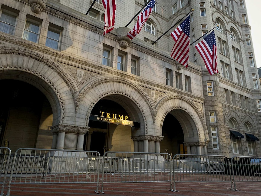 The exterior of the Trump Hotel in Washington DC with US flags and metal fences around the entrance