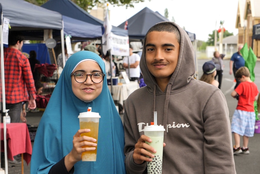Girl and boy holding bubble tea drinks in front of market stalls.