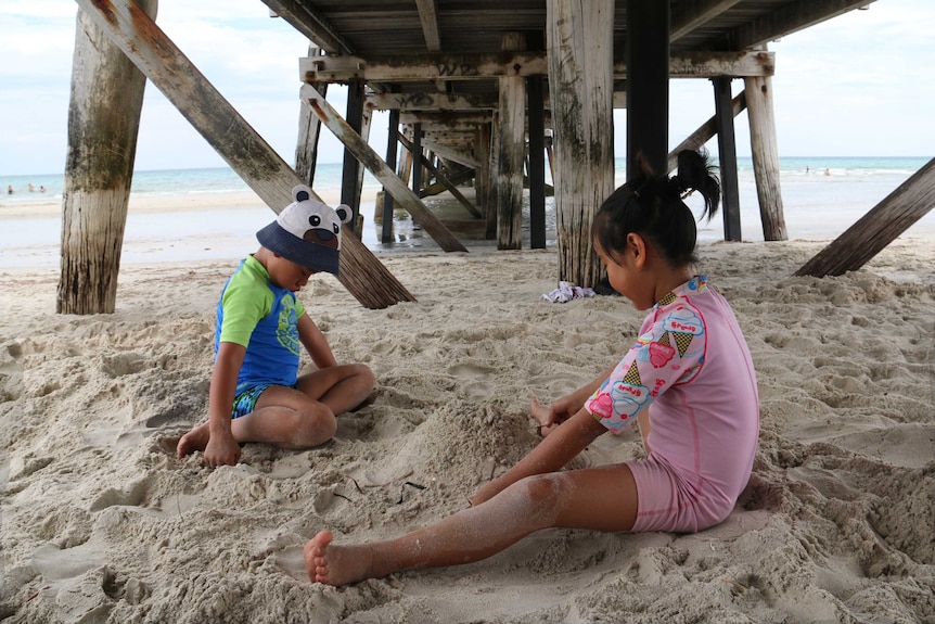 Children play on the sand under a jetty at Semaphore Beach