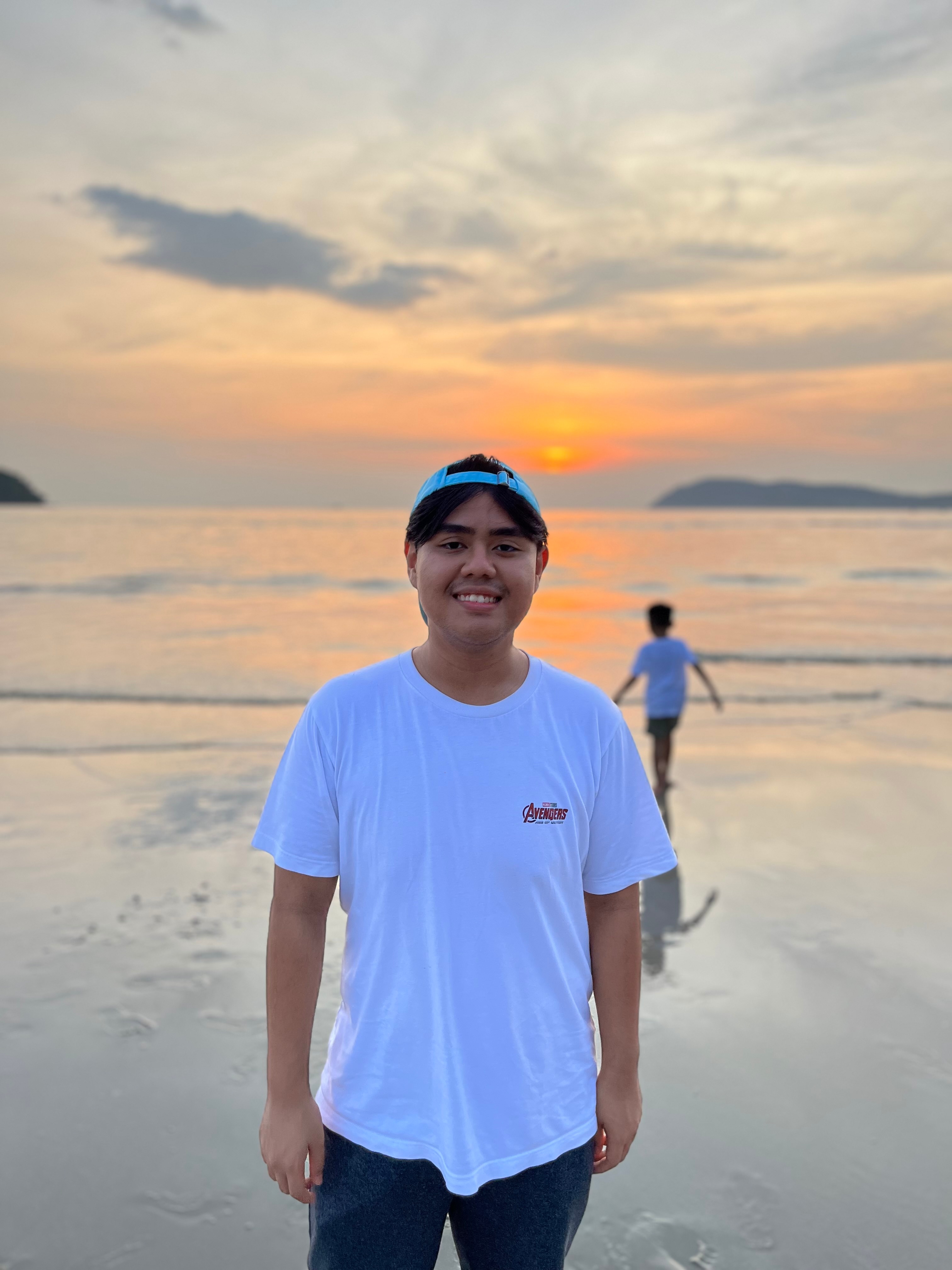 Ayman Hareez Muhammad Adib standing on a beach with a sunset in the background. 