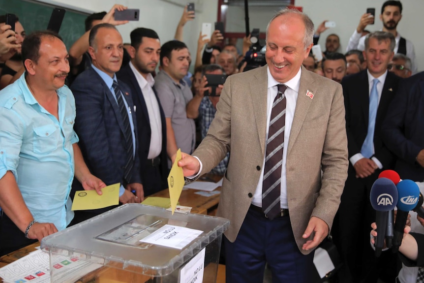 Muharrem Ince puts a yellow piece of paper in a clear box as a room of people watch on.