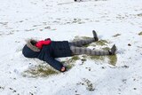 A child lies on a snow-covered ground making a snow angel. 