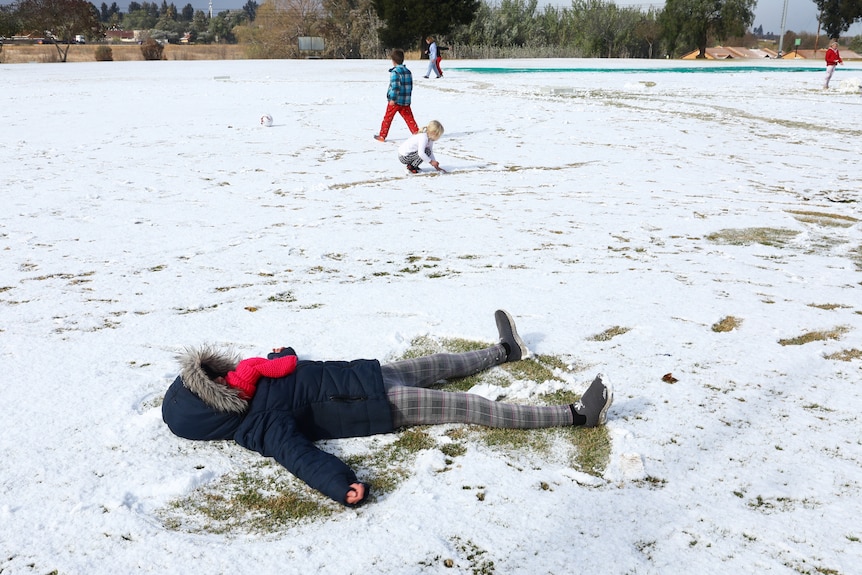 A child lies on a snow-covered ground making a snow angel. 