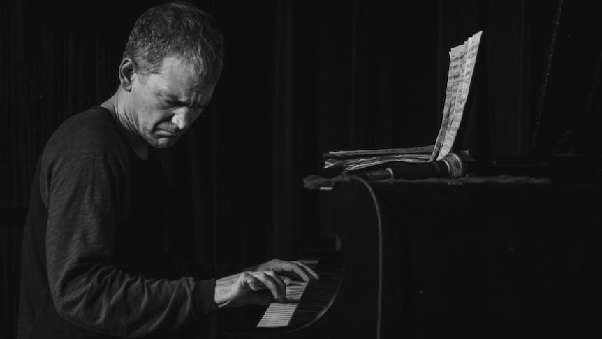 A black and white photo of Brad Mehldau sitting at a piano playing very intently. His eyes are closed.