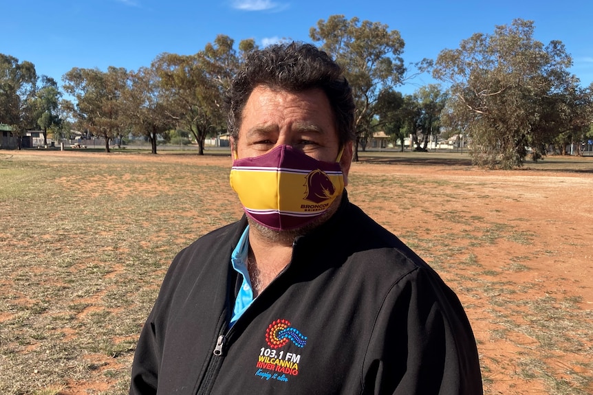 An Indigenous man stands in a field, wearing a mask.