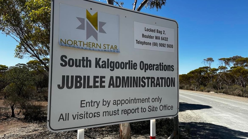 An entry sign for a mine site next to a dirt road   