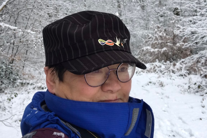 王丽玲站在一颗被白雪覆盖的大树前，头戴黑色宽檐帽