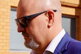 A bald man wearing sunglasses and a blazer