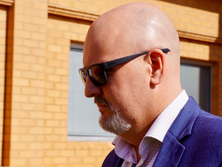 A bald man wearing sunglasses and a blazer