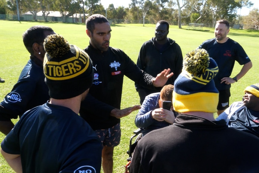 Isaac Trew speaks to a huddle of other Footy 4 Life participants on a football field