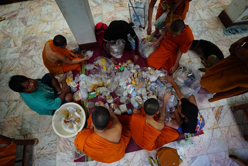 An overhead shot shows a group of people seated while sorting through a variety of food packed in plastic packets