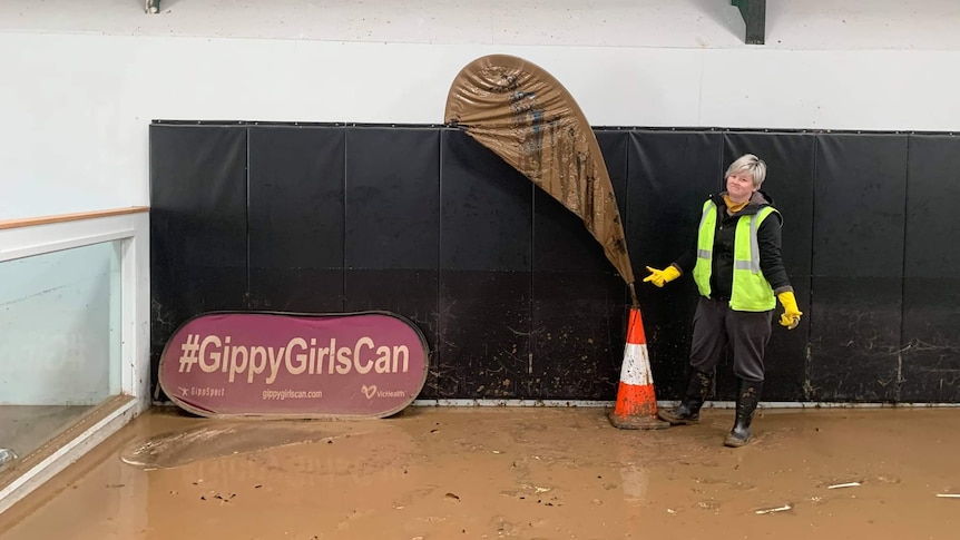 Bodye Darvill is standing on a muddy floor next to a muddy sign saying gippy girls can and safety cone