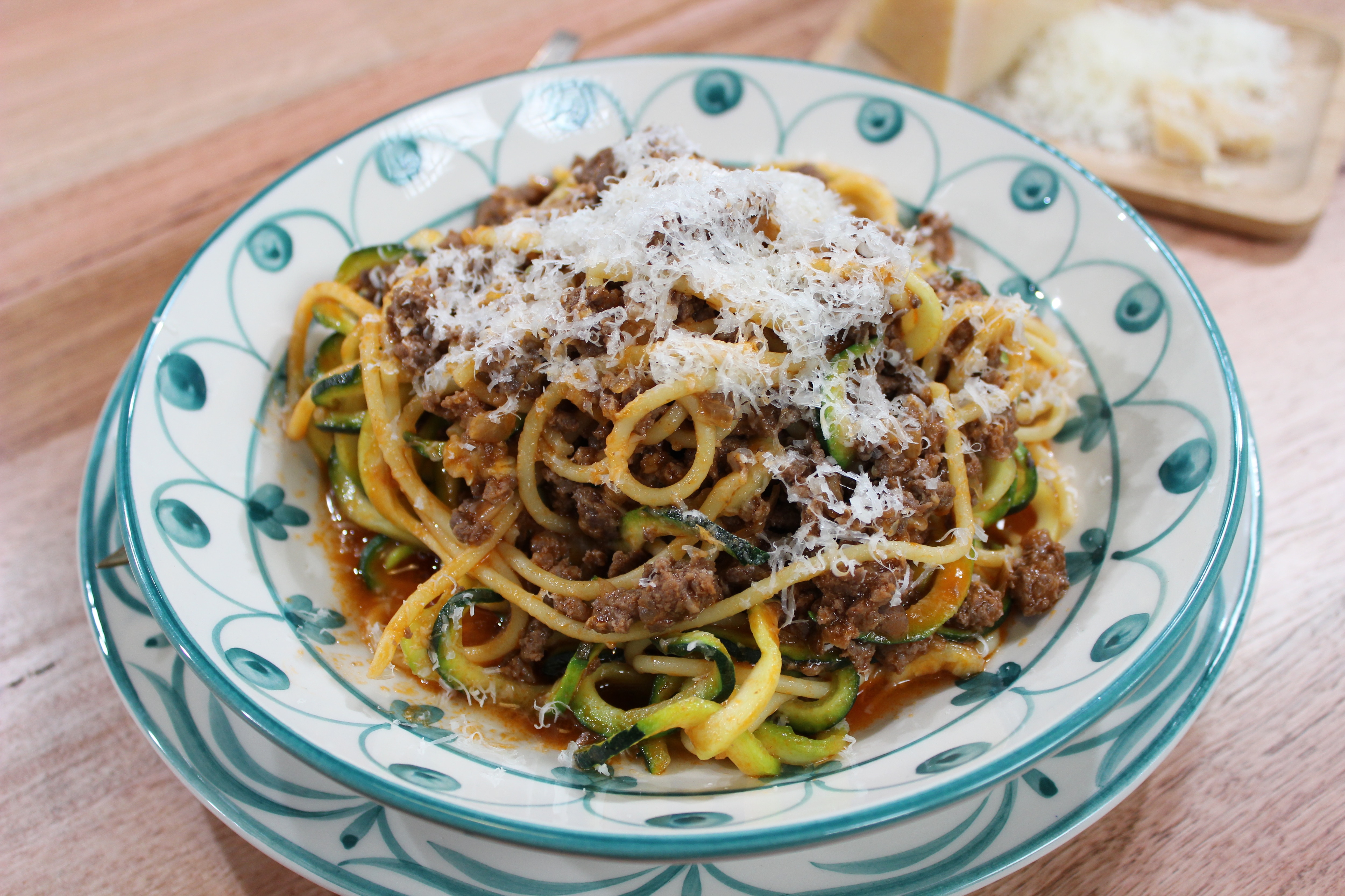 A picture of bolognaise with spaghetti and zucchini noodles in a bowl with grated parmesan on top.