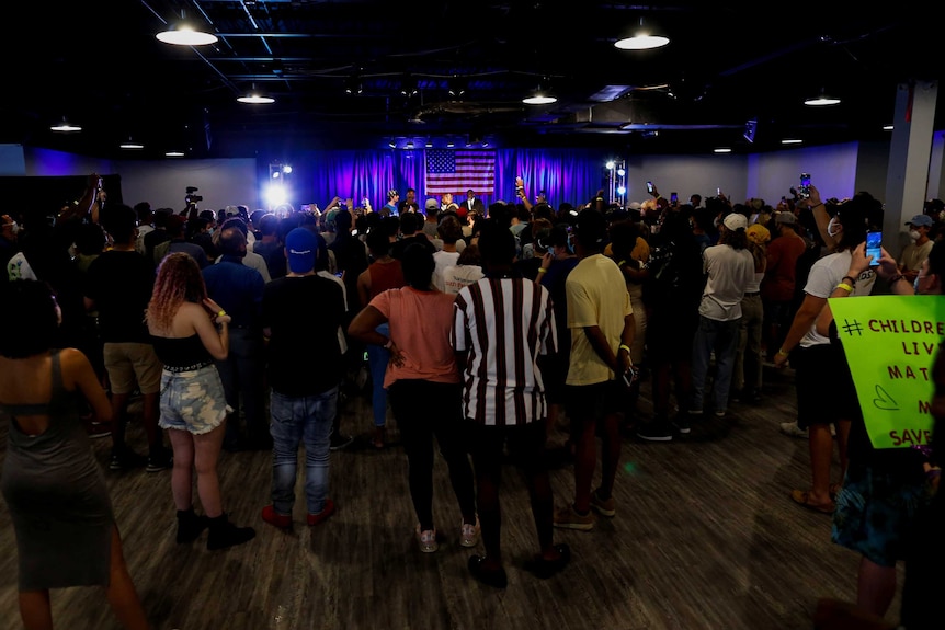 A crowd of a few hundred mostly young adults in a room with Kanye West on stage in the distance