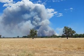 Smoke from a distant grassfire billows into blue sky with bare, brown paddocks in the foreground.  