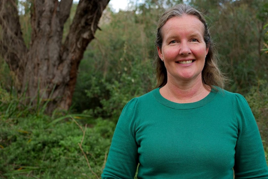 A woman standing  in bushland smiling at the camera
