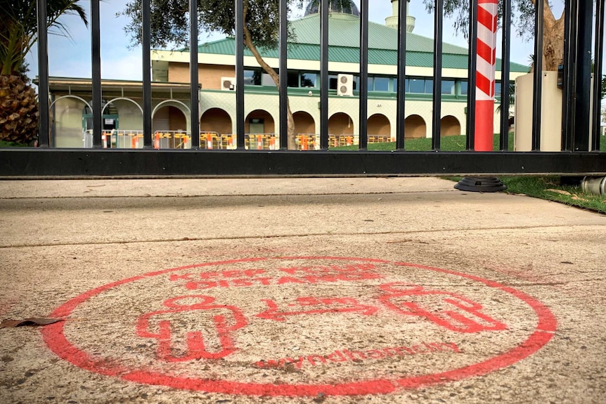 A social distancing sign on the ground in front of the gates of a school.