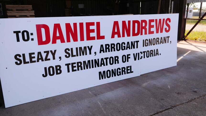 A sign that reads: To: Daniel Andrews. Sleazy, slimy, arrogant, ignorant, job terminator of Victoria. Mongrel.