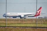 A Qantas plane on a tarmac behind a wired fence.