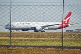 A Qantas plane on a tarmac behind a wired fence.