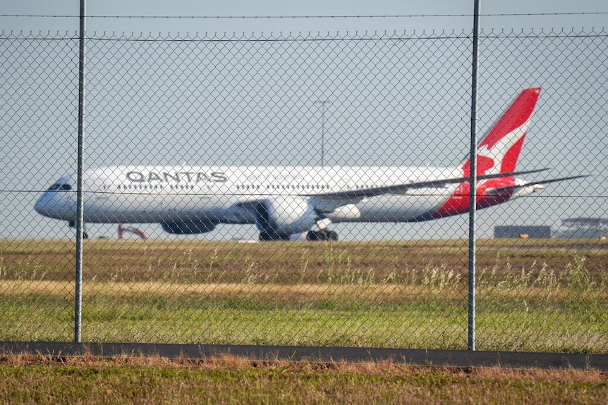 A Qantas plane on a tarmac behind a wired fence.