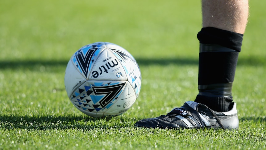 A football next to somebody's boot on green grass