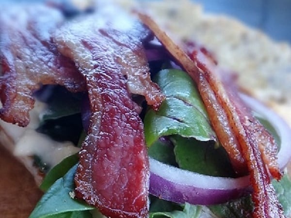 A photo of a sandwich with butter, lettuce and lamb bacon on top.