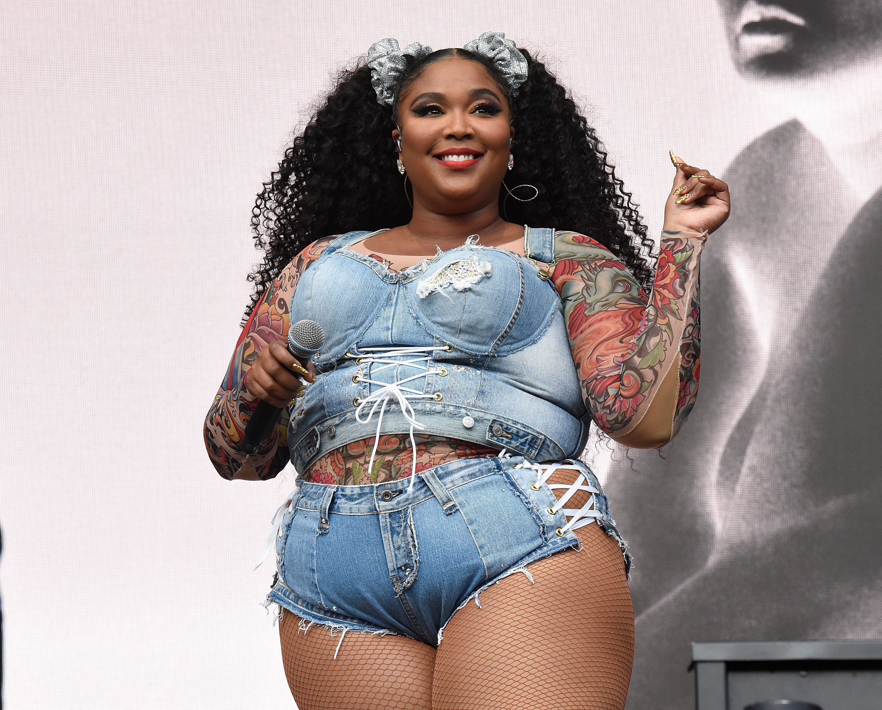 Lizzo dressed in a figure-hugging denim outfit, tattoo sleeve on display