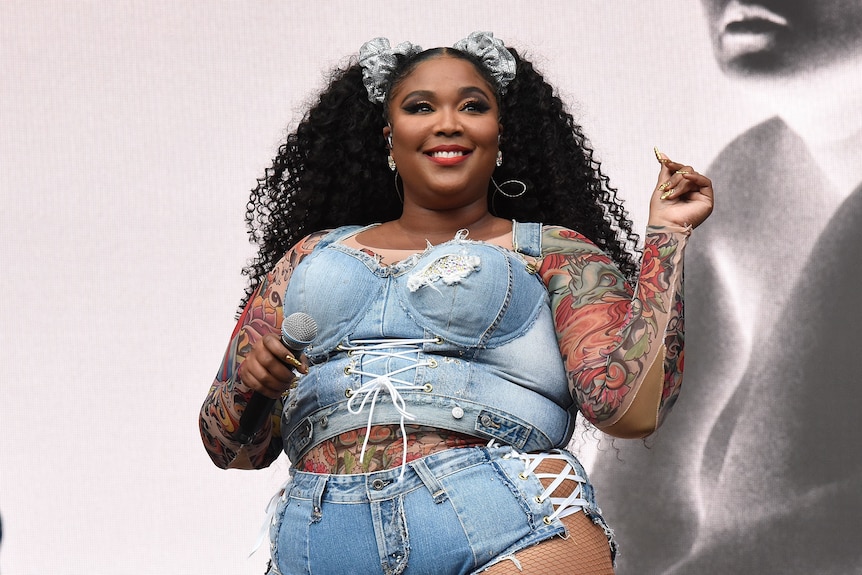 Lizzo dressed in a figure-hugging denim outfit, tattoo sleeve on display