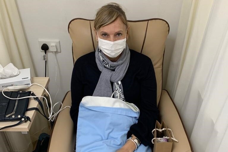 A woman in a face mask sits in a chair in a hospital.
