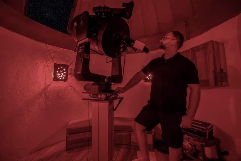 A man stands next to a giant telescope.