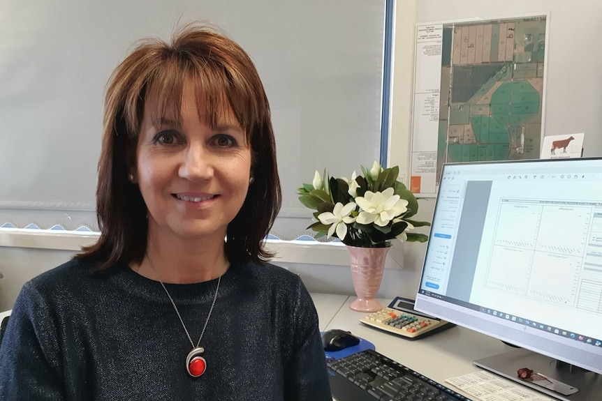 A brown-haired woman smiles sitting next to a computer