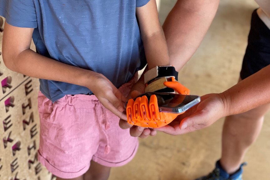 Young girl holding phone in her orange prosthetic hand 