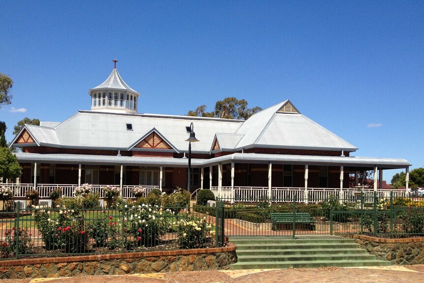 A tin-roofed building with a broad veranda looking out over rose gardens.
